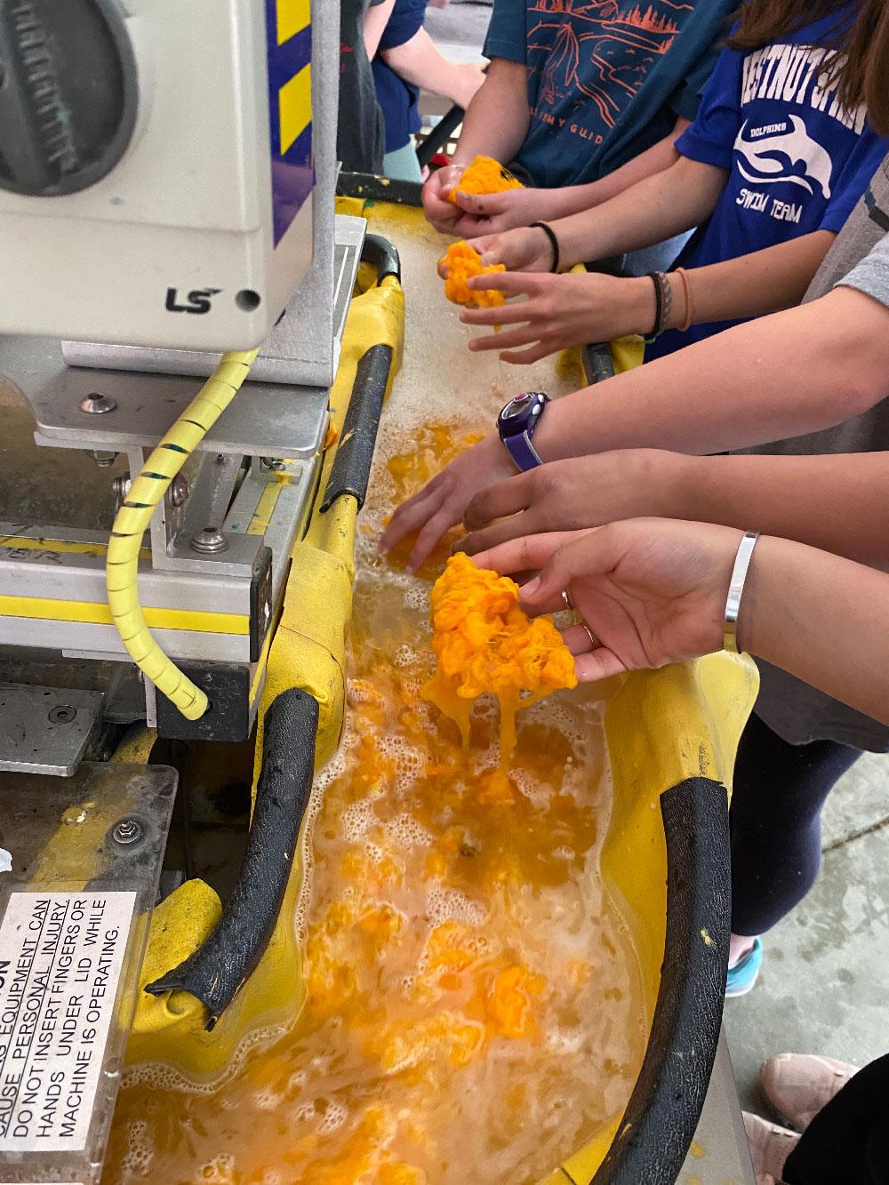 Thesis 4 / A hand using a tool to shape or scrape a thick layer of bright yellow material on a surface.