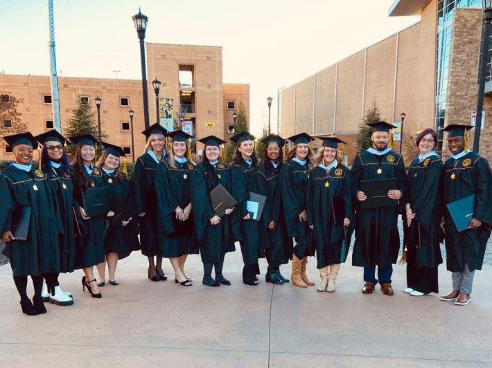 Patsy Rausch with fellow graduates / A group of people wearing graduation gowns and caps gathered together outside a building.