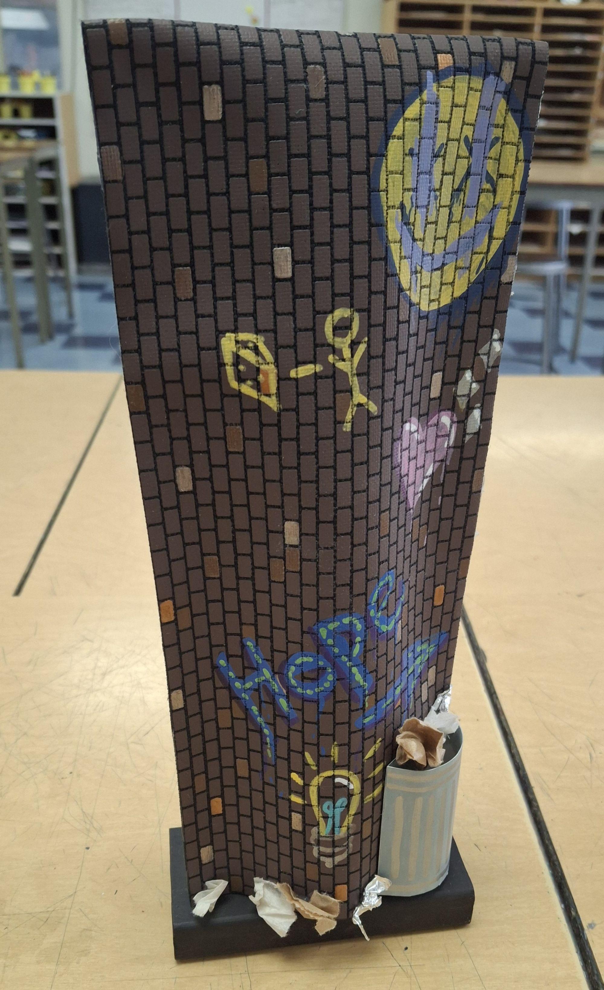 Miniature brick wall with graffiti, a trash can, and crumpled paper in an indoor setting.  / Sound suit example for Sculpture 2 class. This lesson allowed students to expand on their previous knowledge of sewing.