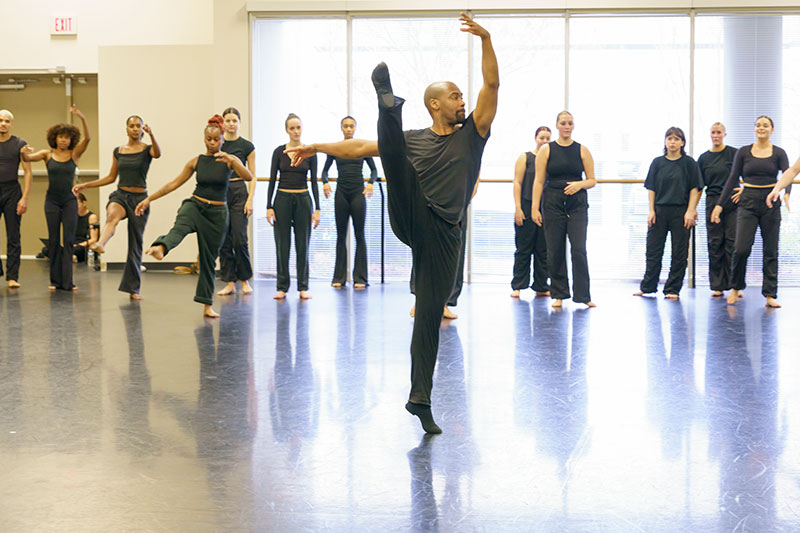 Dancer in ballet pose in studio with many students