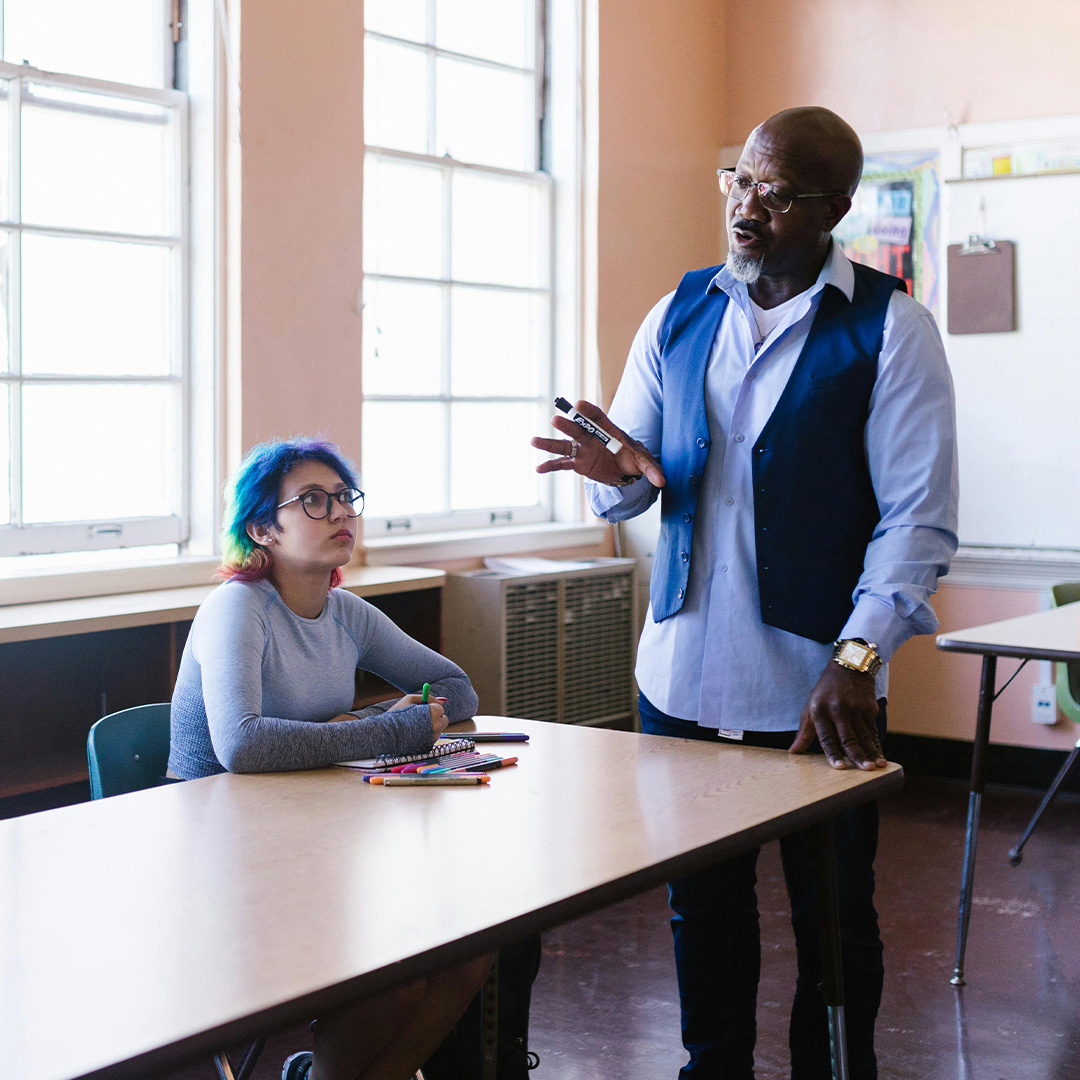 male teacher standing up and lecturing to students at desk