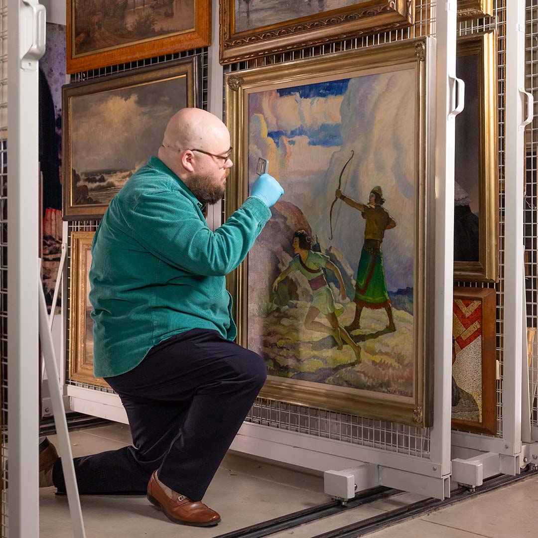 middle aged man examining painting in museum storage