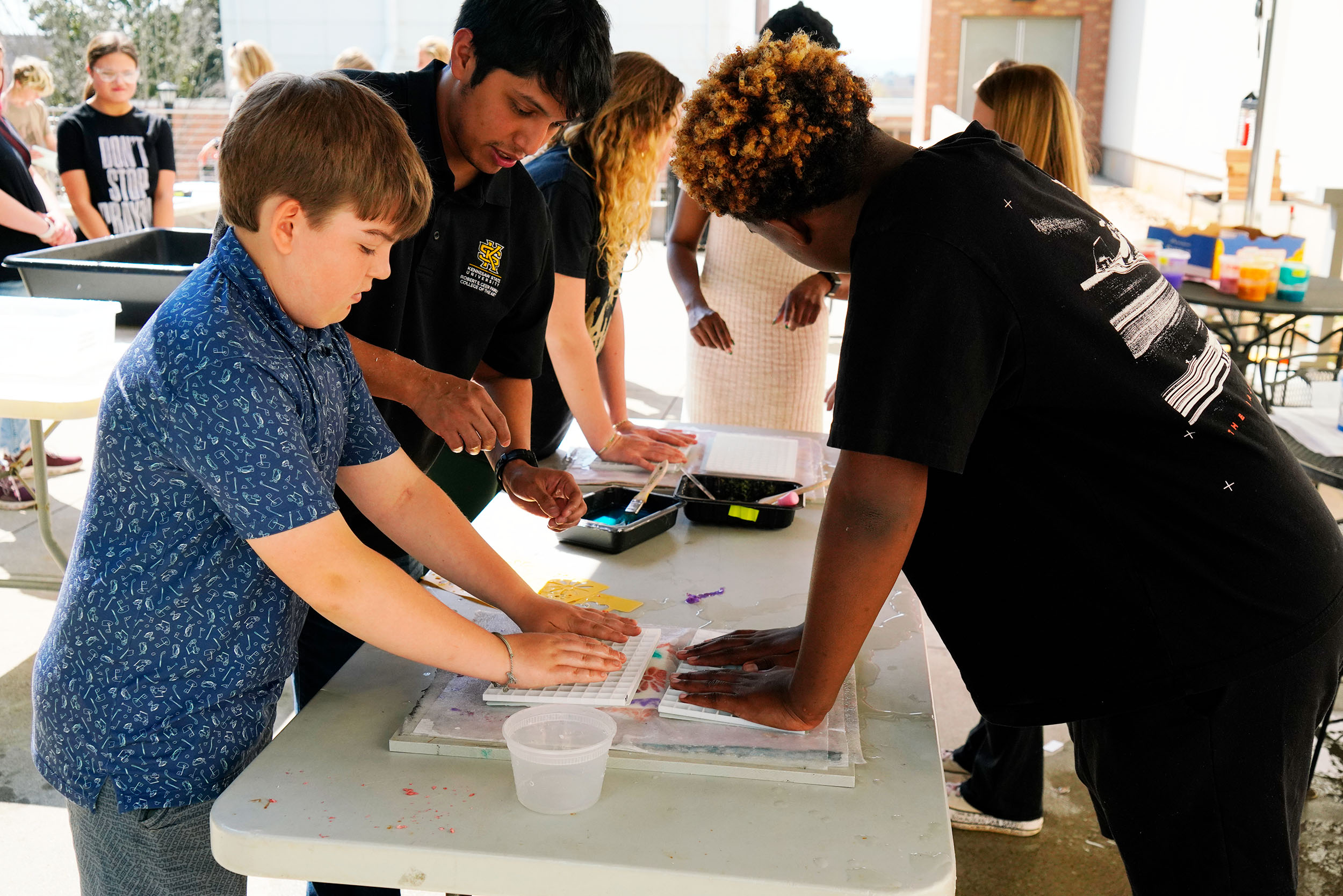image of a man helping two younger children with a papermaking workshop outside 