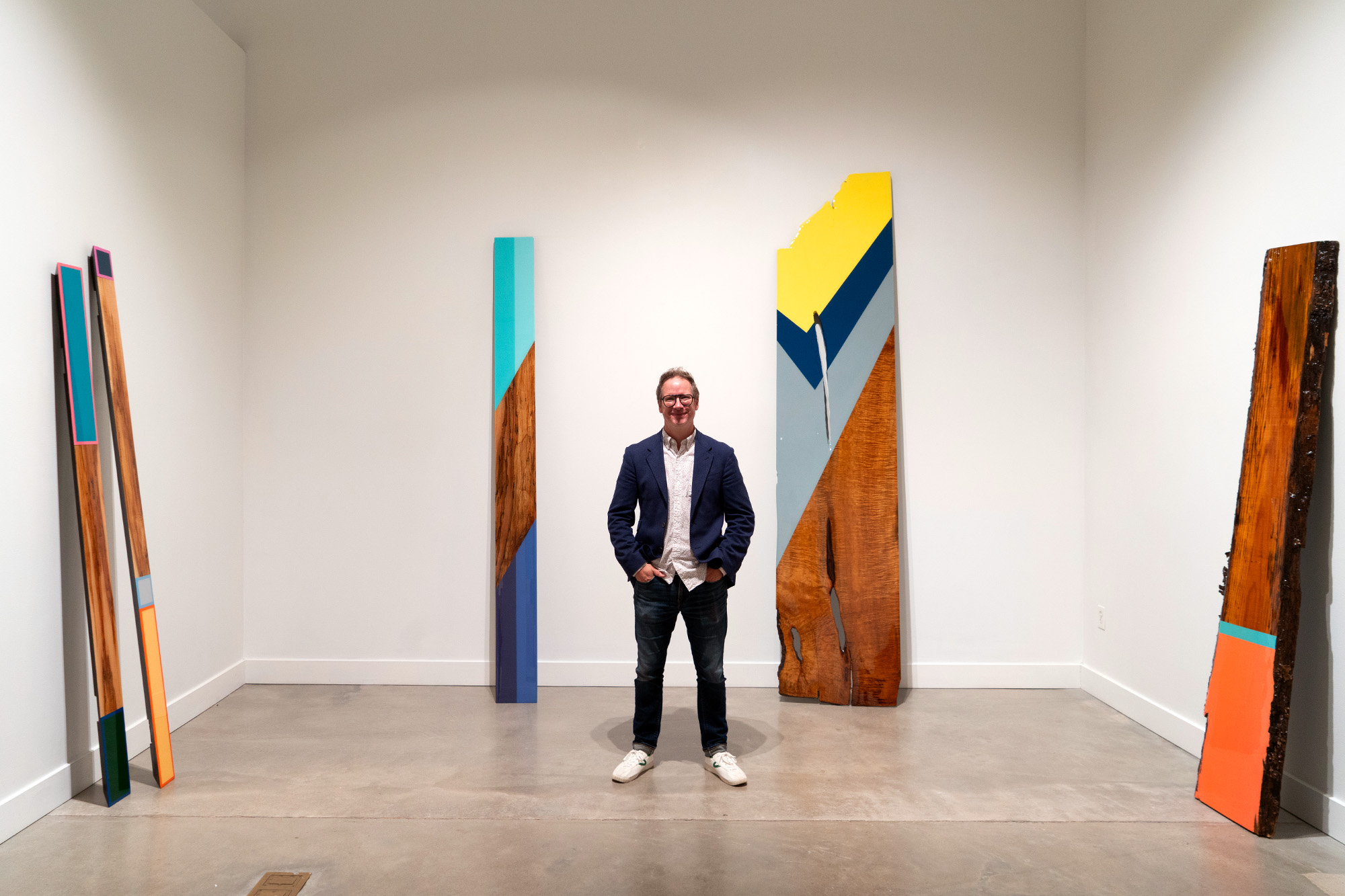 man standing in front of large wooden scupltures with color and paint on them