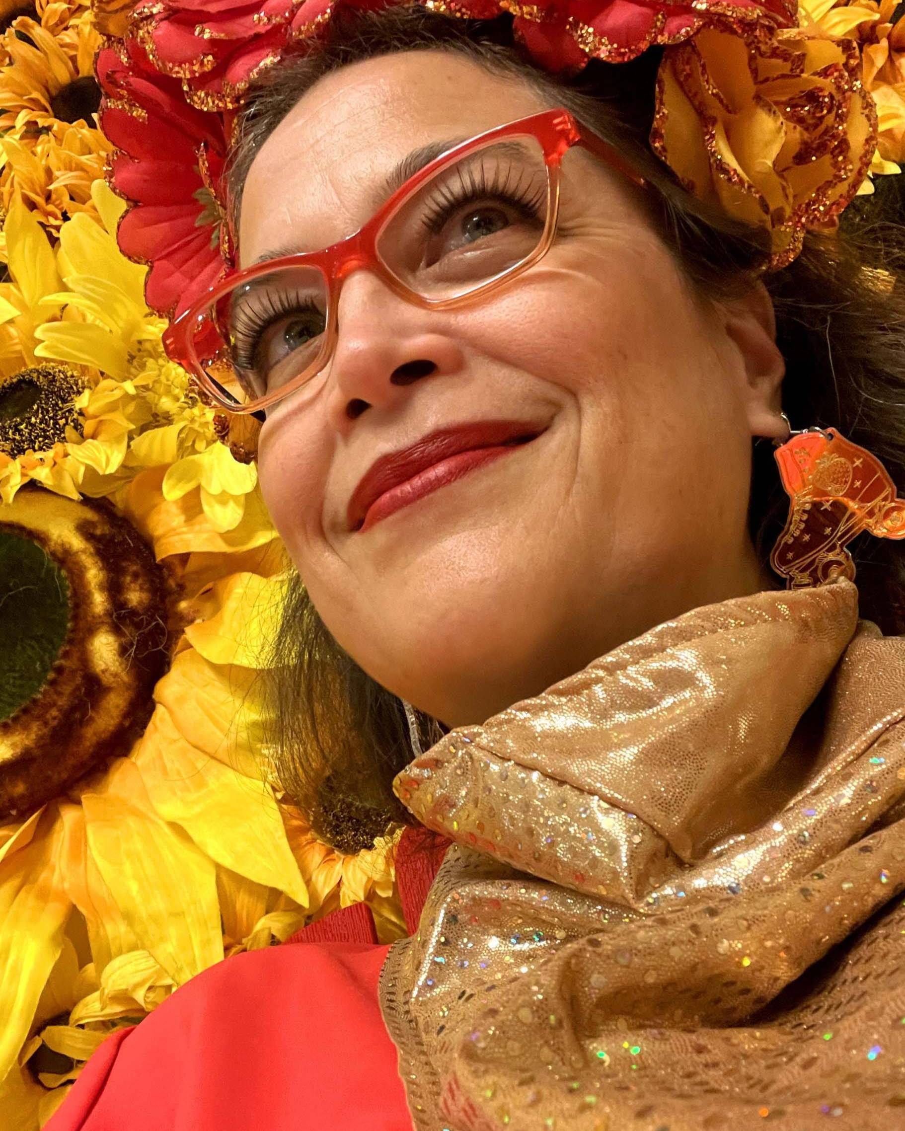 headshot of female artist with flowers in her hair in front of warm floral background