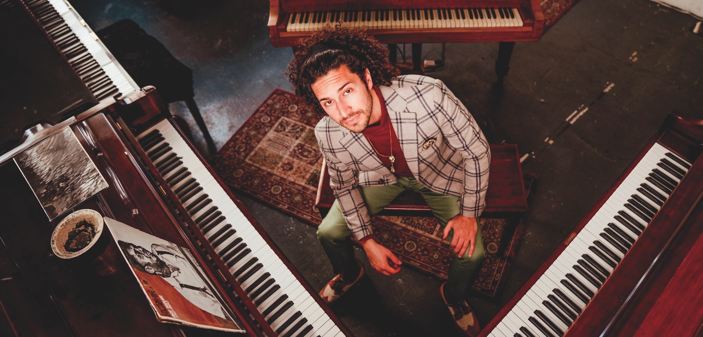 Emmet Cohen looks up at camera while surrounded by keyboards