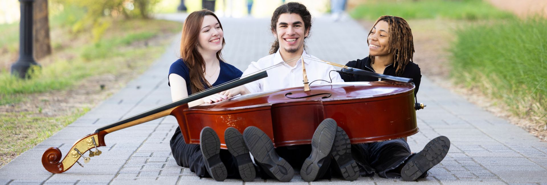 three_students_sitting_on_ground_with_bass