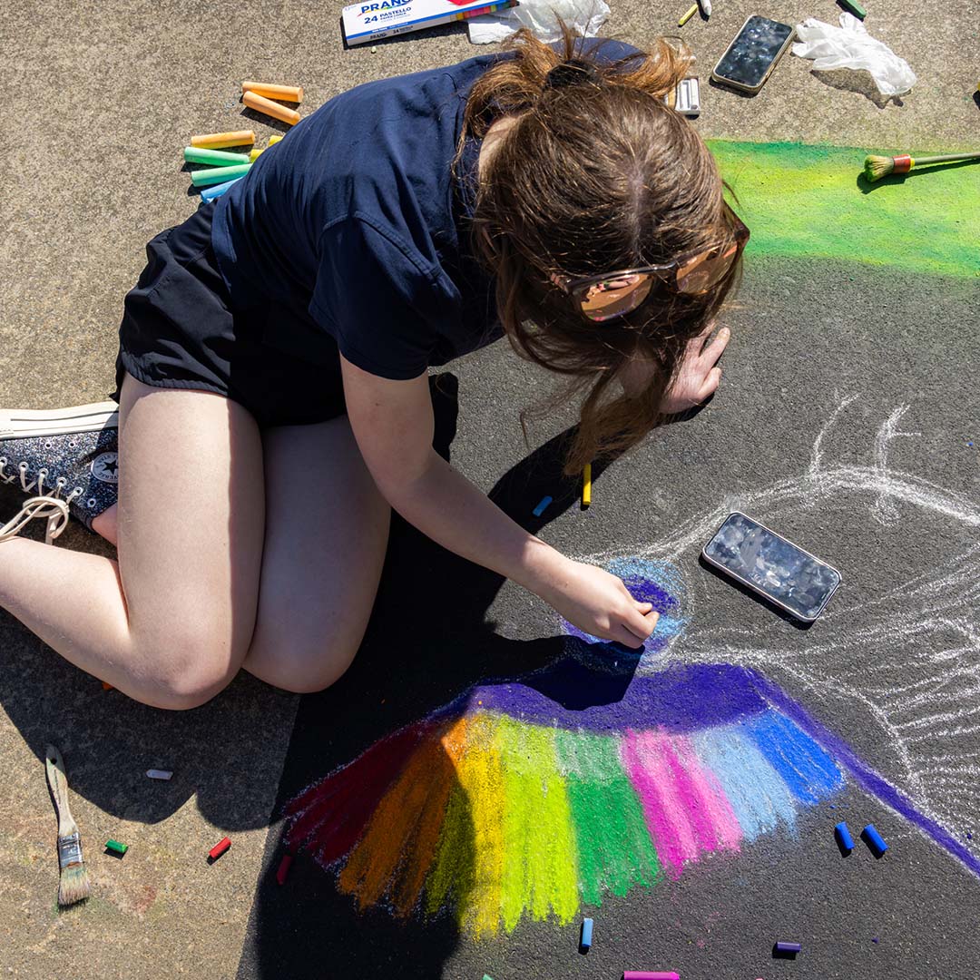 girl chalk drawing rainbow bird on concrete