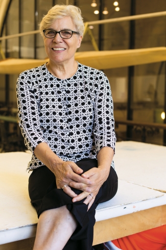 headshot of an older woman sitting on a sewing table and smiling