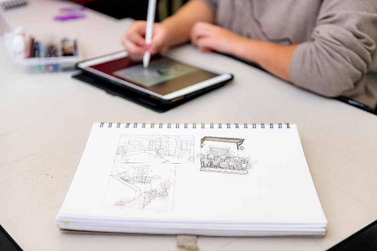 student drawing on ipad and sketches in notebook