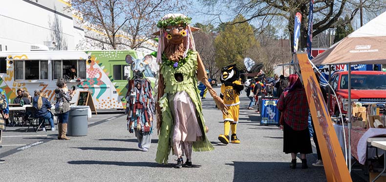 Scrappy the mascot parading through artist market with giant colorful hand crafted puppets