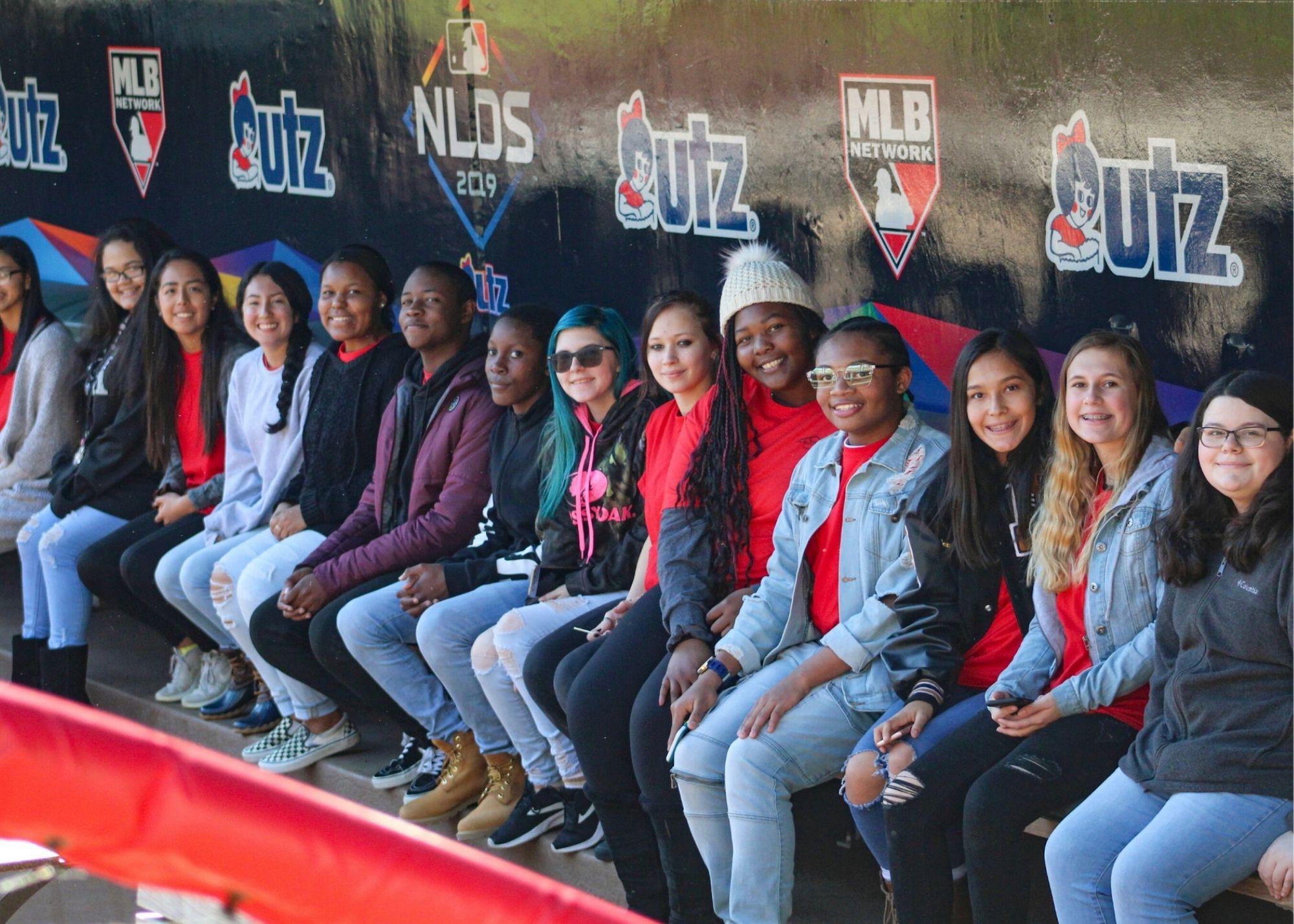 Students smiling and sitting in front of a wall painted with the MLB logo and UTZ logo.  / KSU TRiO Upward Bound at Rockmart and Cedartown High Schools visit the Suntrust Park to learn about stadium construction and architecture. 