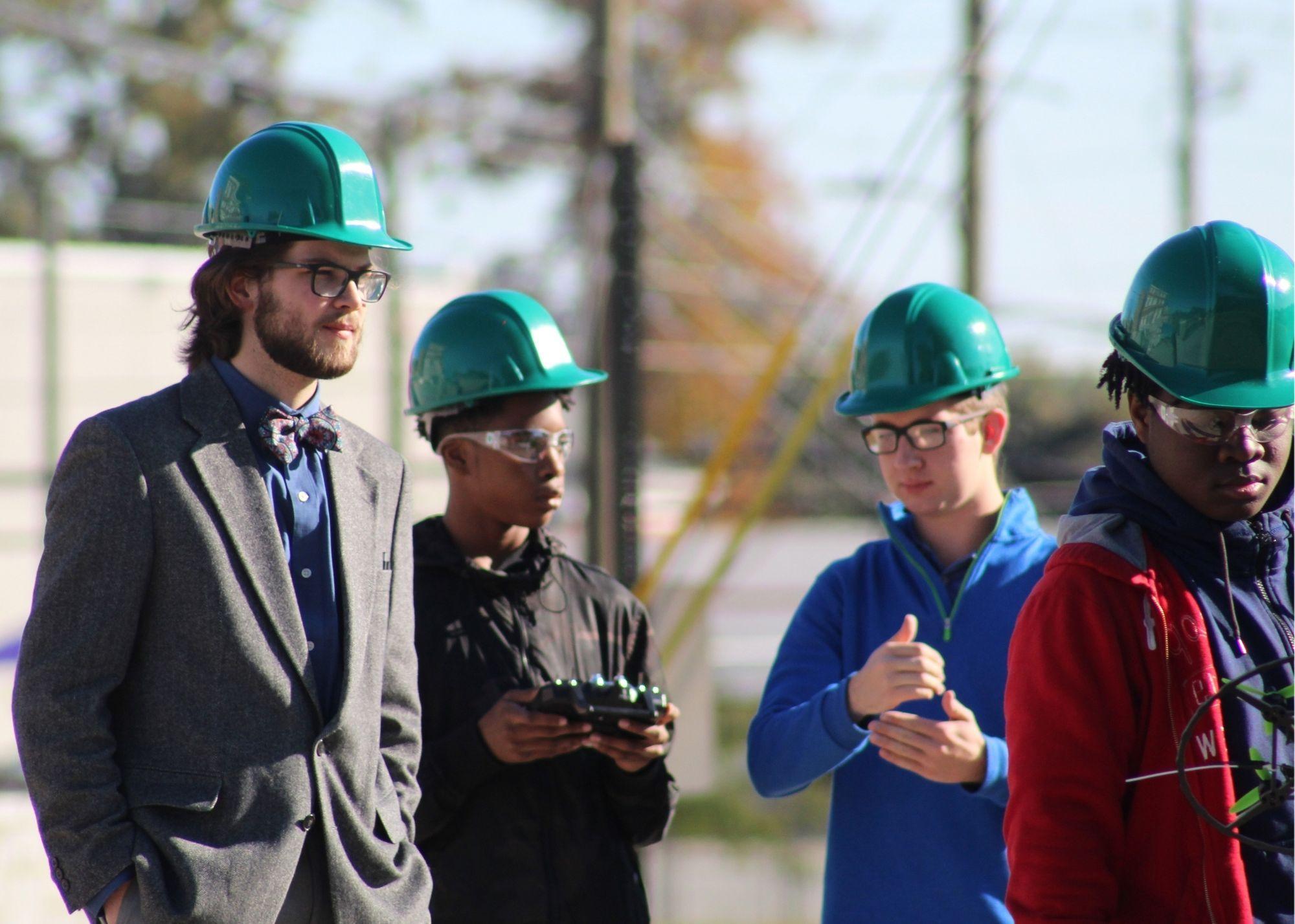 Four students wearing hardhats, with one holding a remote control and another holding a drone.  / KSU TRIO's groundbreaking Drone Program introduces students to the basics of drone flying, ethics, and mechanics, and the program gives students the opportunity to test for their FAA Pilot's License 