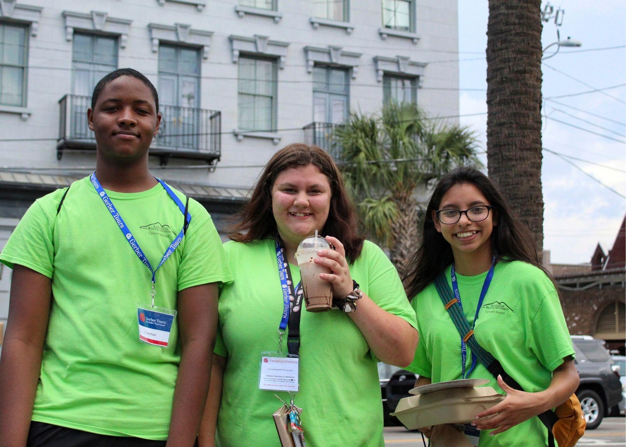 Three students smiling, wearing green shirts standing outside in front of a white building.  / KSU TRIO Students have the opportunity to go on an out of state, educational field trip after full participation in the KSU TRiO Summer Academy. The trip is provided at no cost to students. 