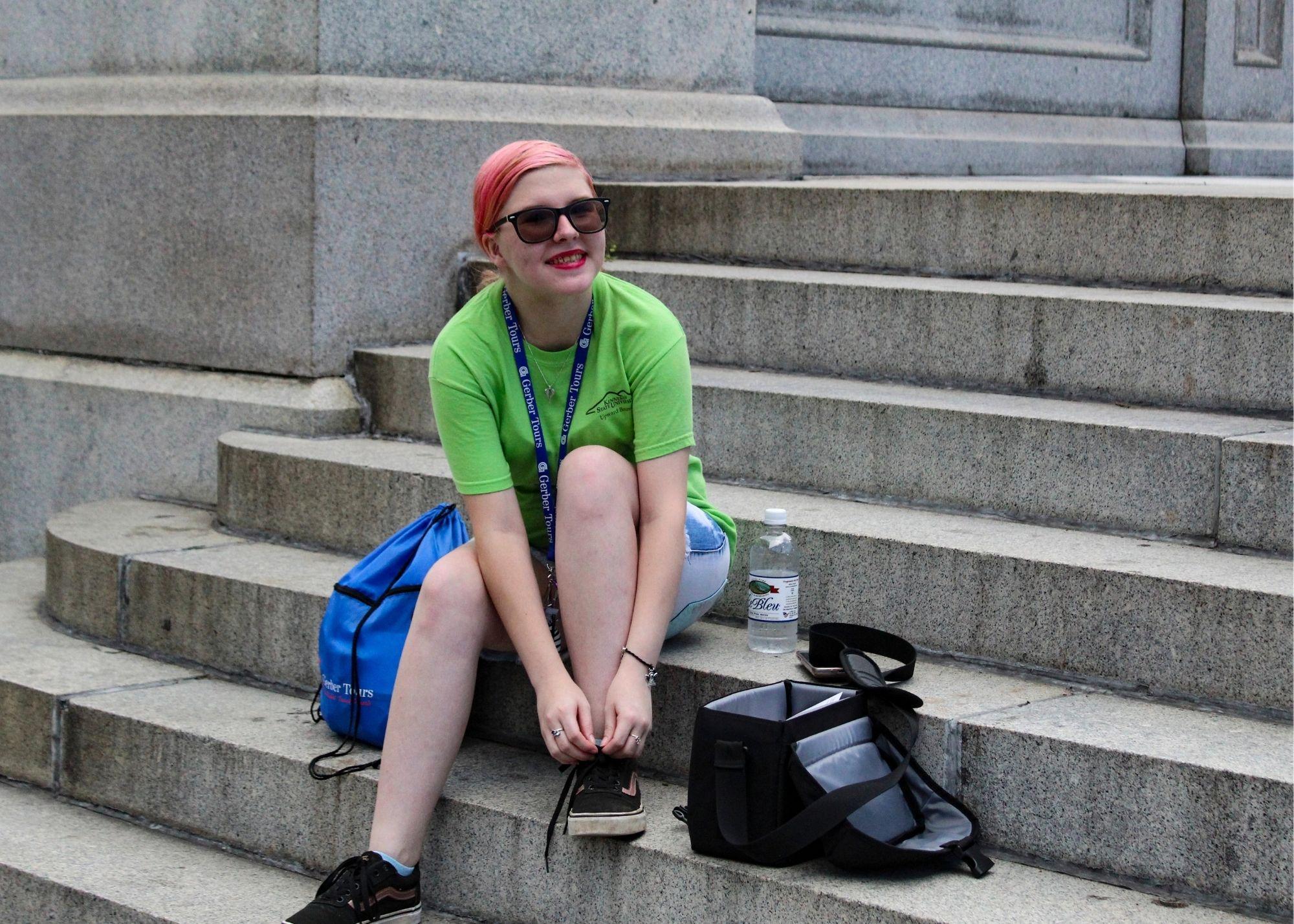 A woman sitting on a set of stairs holding her shoelaces.  / KSU TRiO Upward Bound at Rockmart and Cedartown High Schools visit the Atlanta Zoo. 