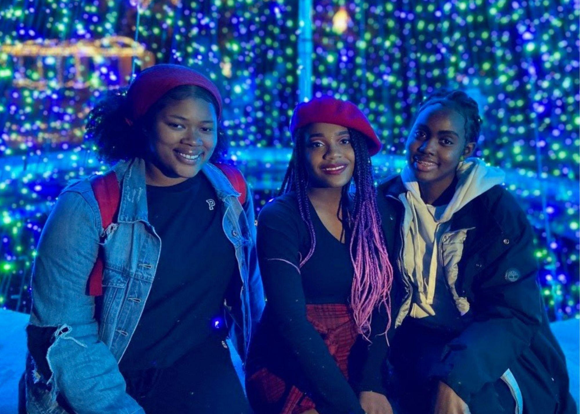 Three students smiling, while in front of a light display at Atlanta Botanical Gardens. / KSU TRIO Students have the opportunity to explore and learn about the science behind the Atlanta Botanical Gardens.