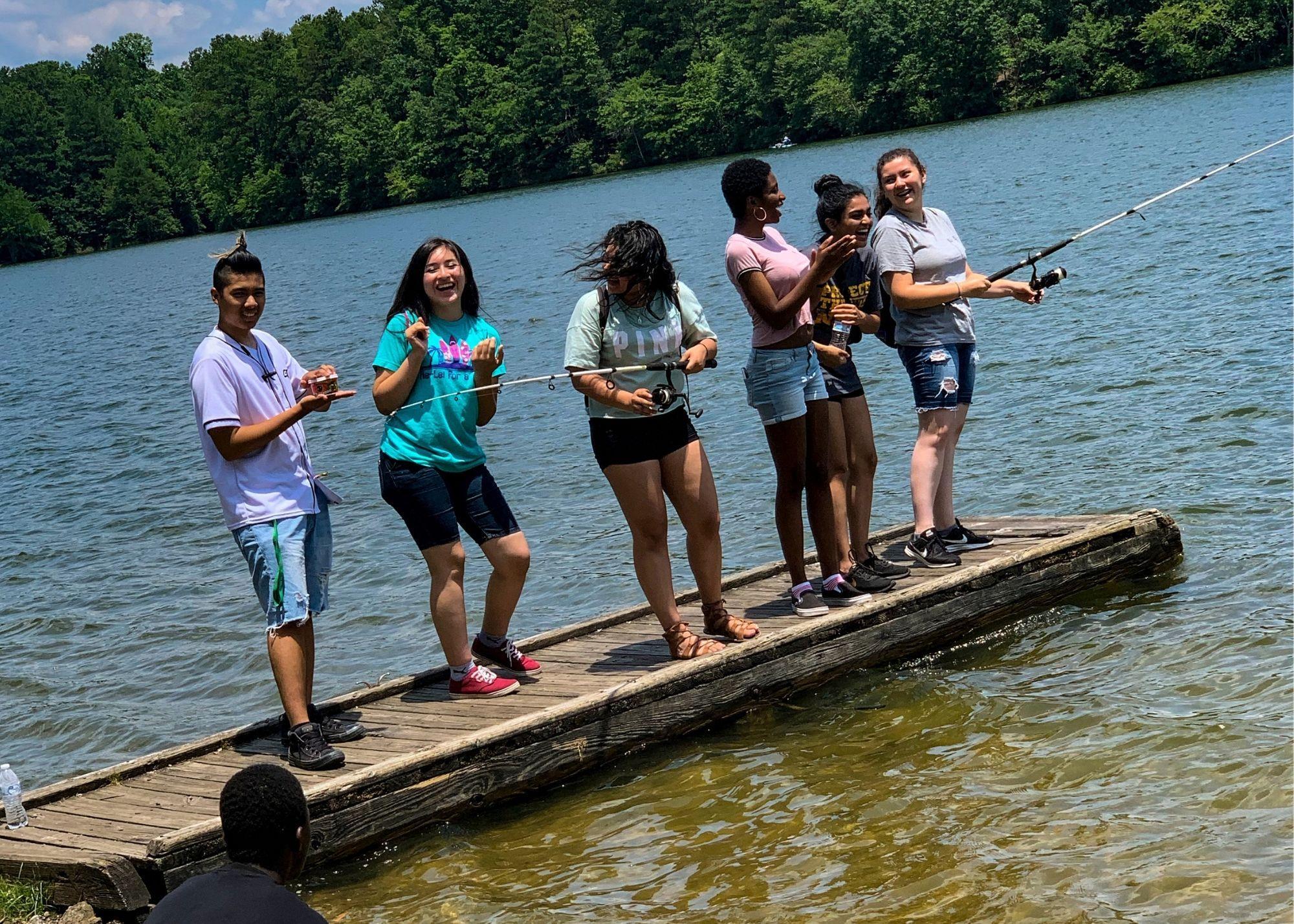 Students standing on a wooden pier, holding fishing rods and fishing.  / Hiram High School Upward Bound learns about ecological preservation.