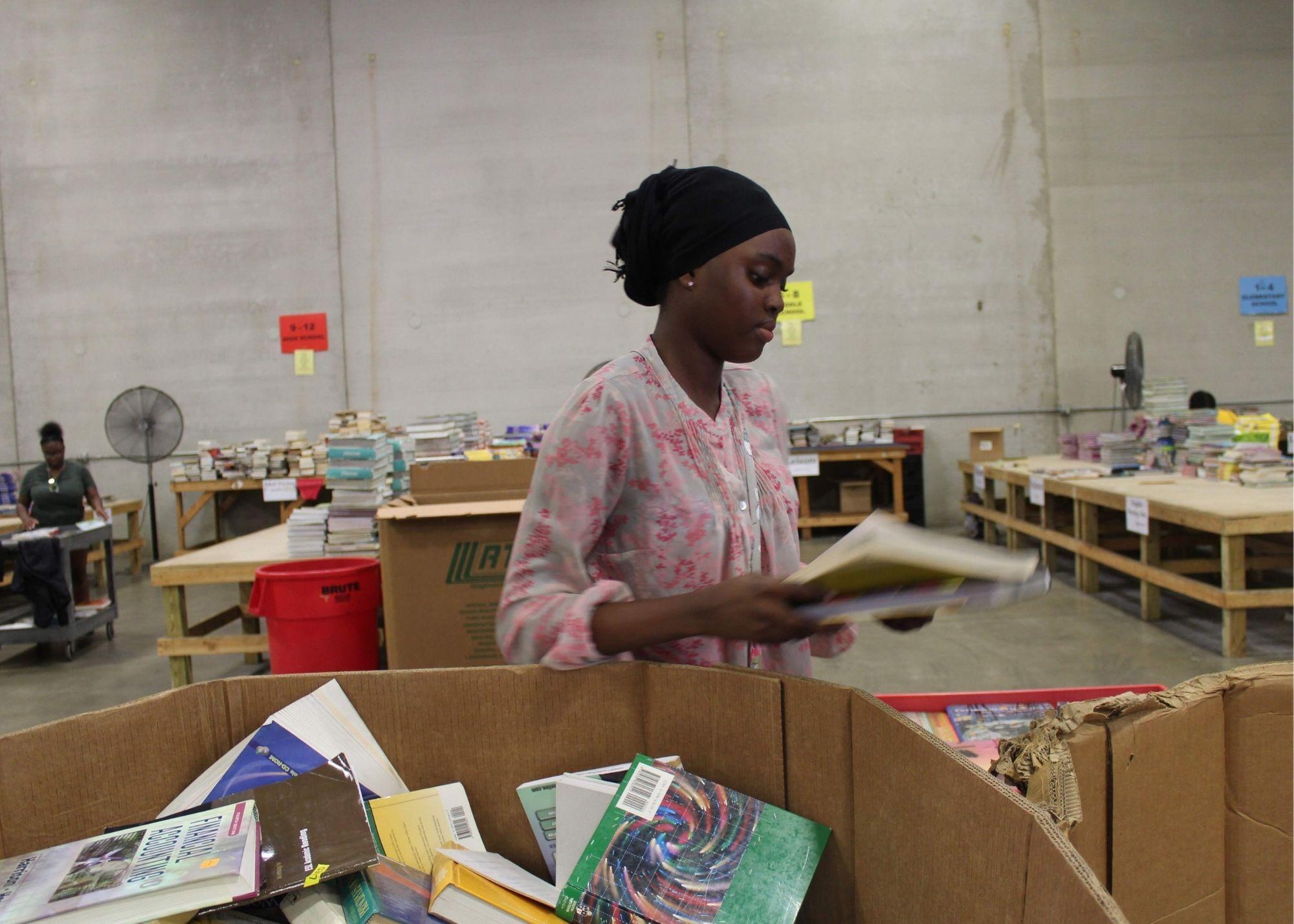 A woman at a book drive event holding books.  / KSU TRiO students give back to the community through a book drive event. 