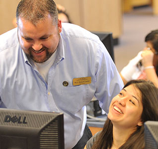 A smiling instructor and student look at a computer, illustrating partnerships and community engagement at Bagwell College of Education.