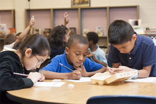 Classroom scene with children writing at a table, emphasizing early childhood education principles from Bagwell College of Education.