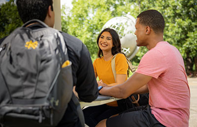 Three KSU students engaged in conversation while seated at a table, sharing ideas and collaborating on their studies.