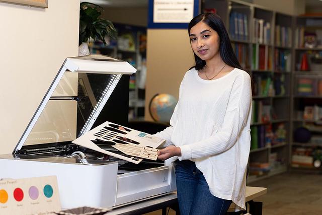 A woman in a white sweater holds laser-cut designs in a makerspace.
