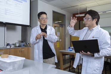 Two boys standingin classroom talking reasearch