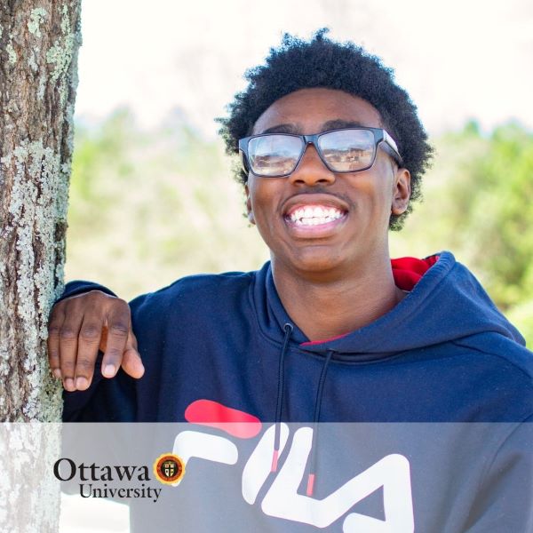 Daniel Blount, a smiling student standing next to a tree, with the Ottawa University logo in the bottom left corner.