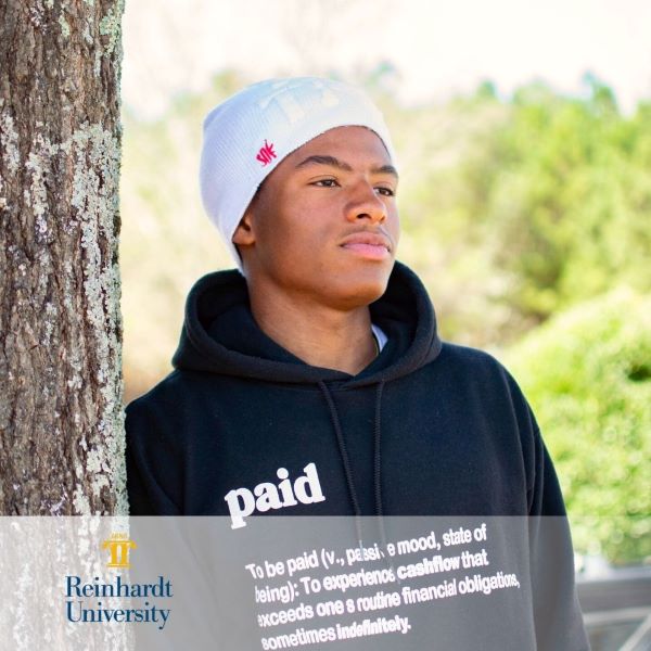 D'Juan Perkins, student standing by a tree with the Reinhardt University logo in the bottom left corner.