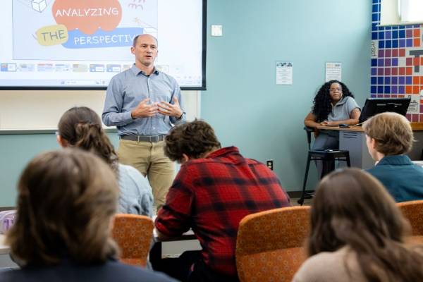 An instructor stands at a podium presenting to an audience of students.