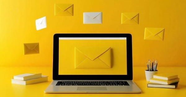 Laptop on a yellow desk with floating yellow and white email envelopes.