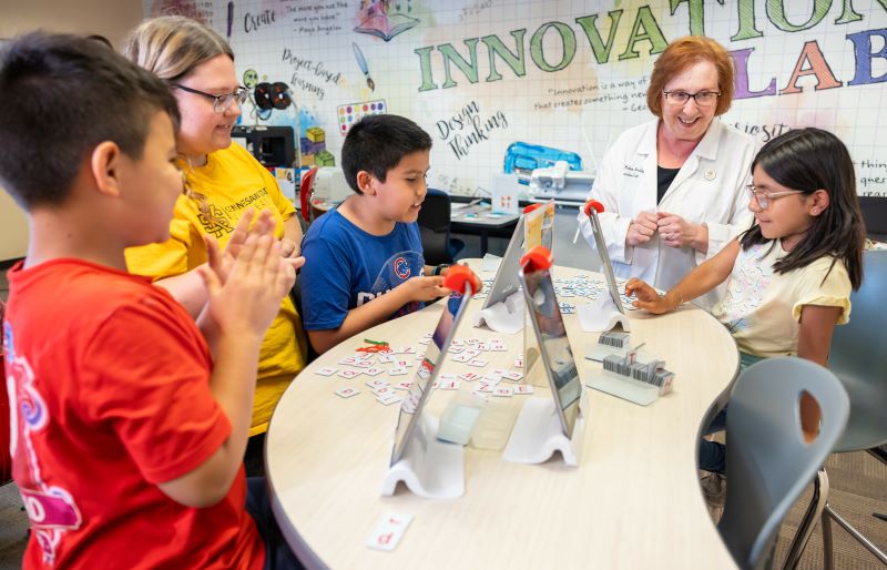 A diverse group of children and a teacher, are gathered around a table, engaging in a collaborative setting.