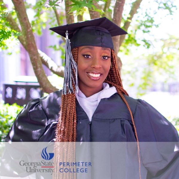 Jaida Anderson, a smiling student in a cap and gown, standing by a tree.