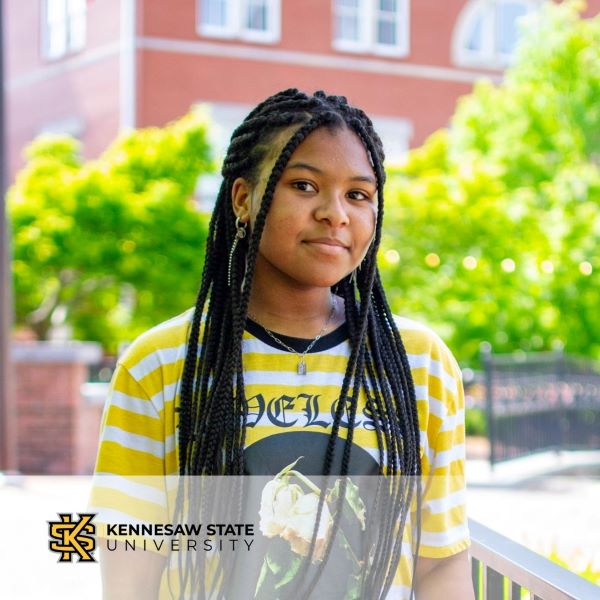 Jayla Lucas, a student dressed in a yellow and white striped shirt in an outdoor setting and with the Kennesaw State University logo in the bottom left corner.