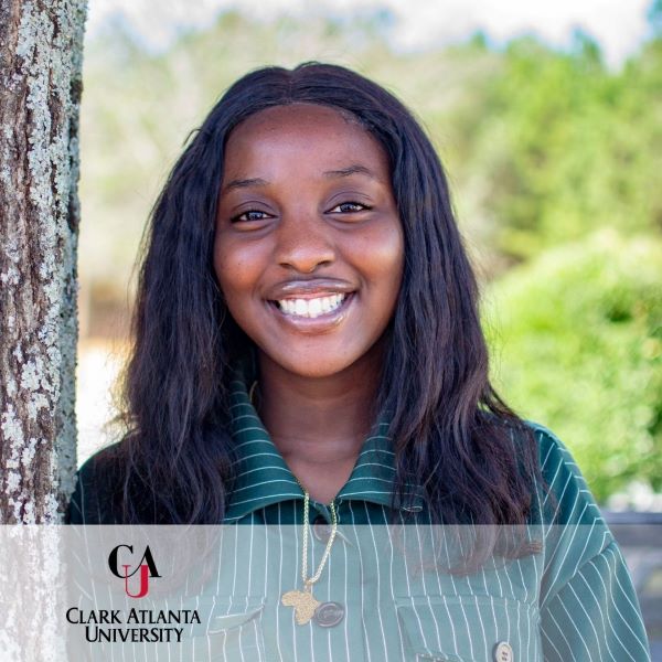 Adeola Ogunderu, a smiling student standing next to a tree with the Clark Atlanta University logo in the bottom left corner.