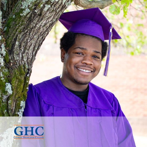 Malik Bullock, a smiling graduate wearing a purple cap and gown, with the Georgia Highlands College logo in the bottom left corner.