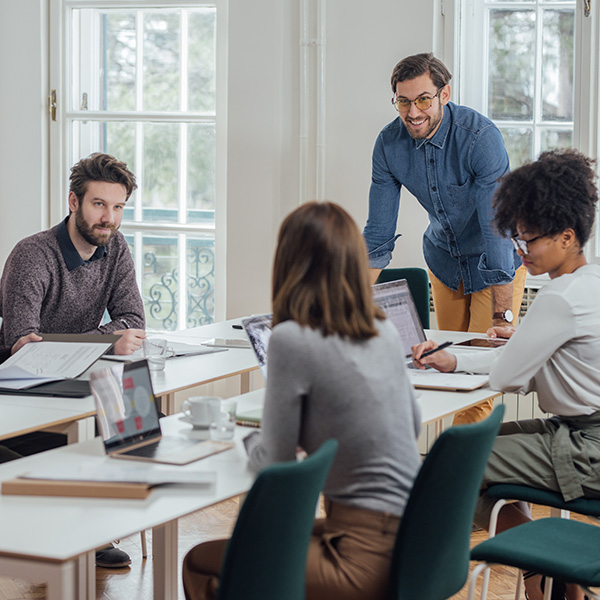 man in denim shirt leaning over table talking to students