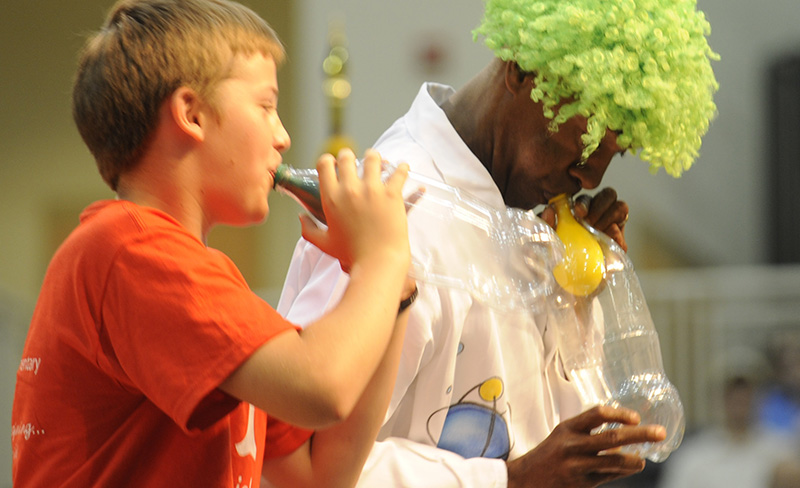man in green wig and small boy blowin up baloons