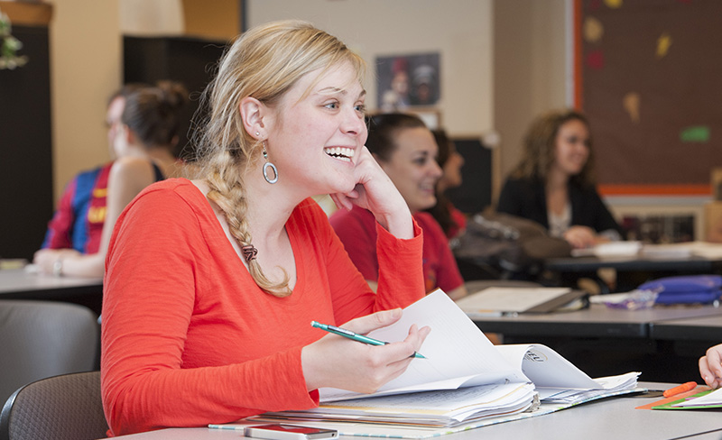 woman in orange shirt taking notes in class