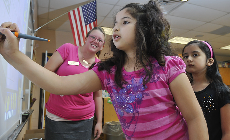 young girl writing on white board with teacher watching