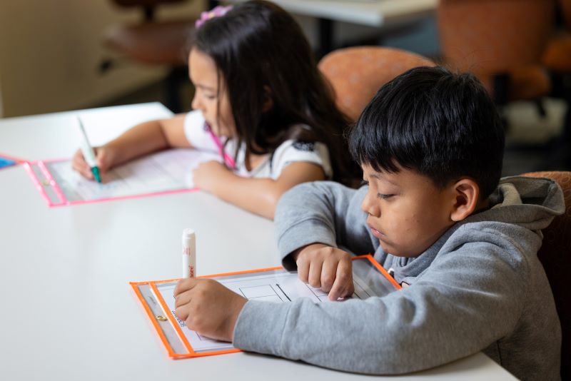 Two students participate in a writing activity in a classroom setting.