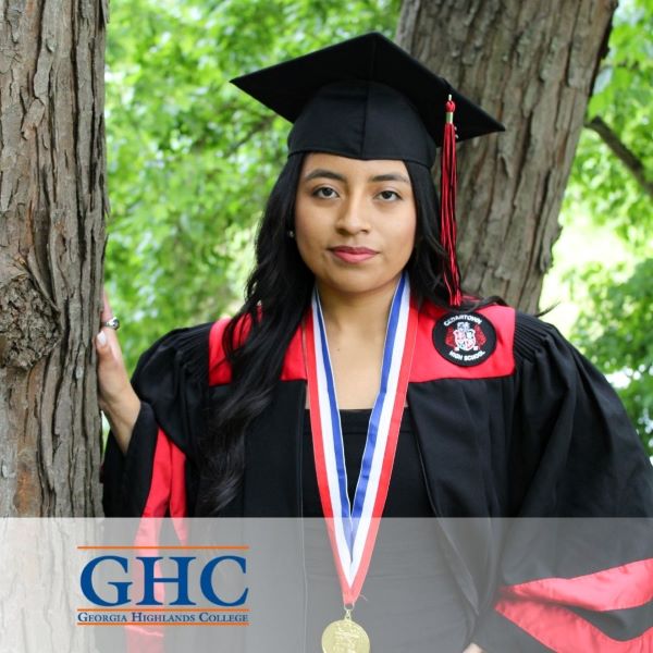 Yoselyn Martinez, a graduate in a cap and gown, standing in front of a tree with the Georgia Highlands logo in the corner.