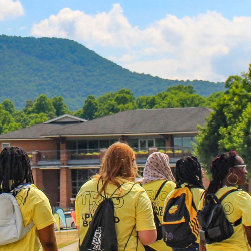 Students in gold KSU TRIO shirts walking past a building, symbolizing the unity and growth fostered by KSU TRIO Families.