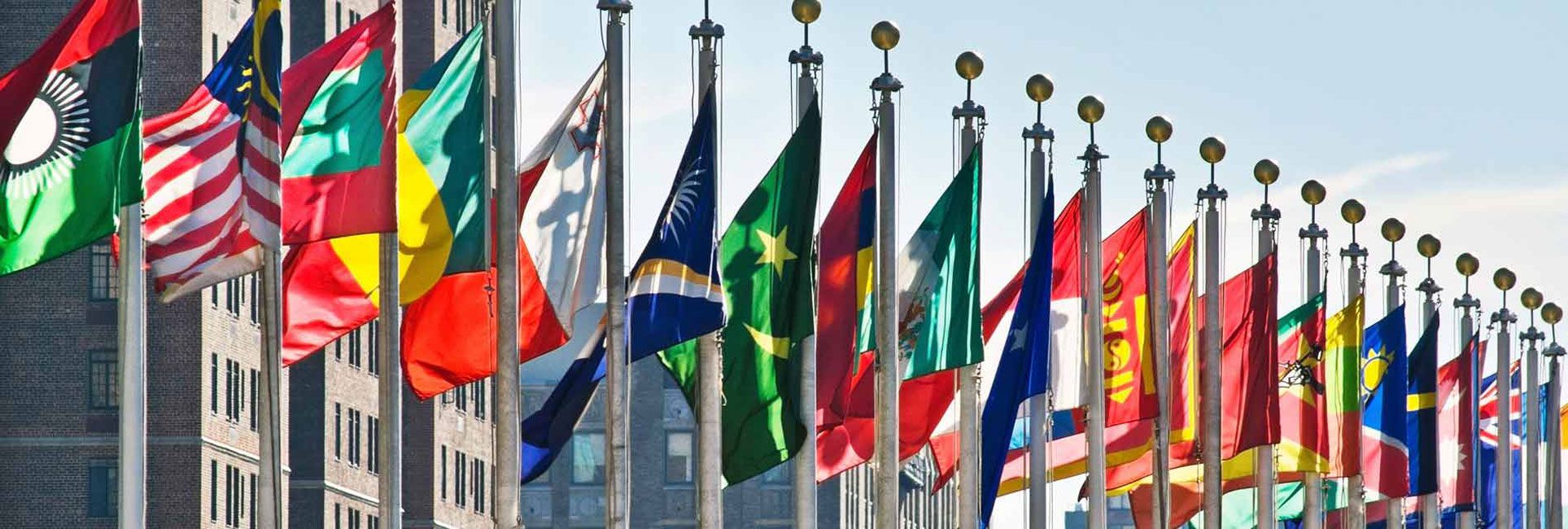 Flags of various nations are displayed in front of a building, highlighting the International Student Teaching Study Abroad initiative.