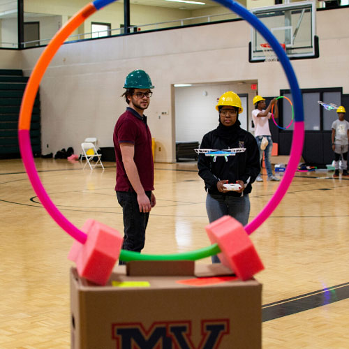 students flying drones in gym