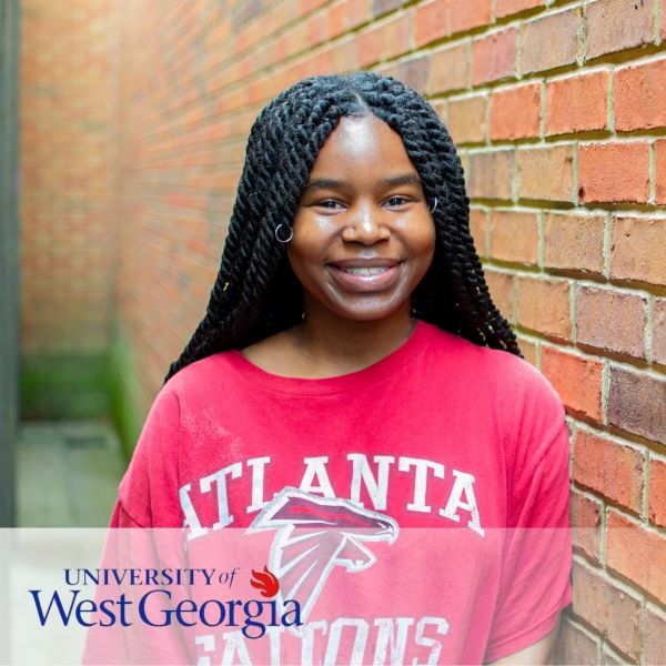 Amber Chaney, smiling and leaning against a brick wall, with the University of West Georgia logo in the bottom left corner.
