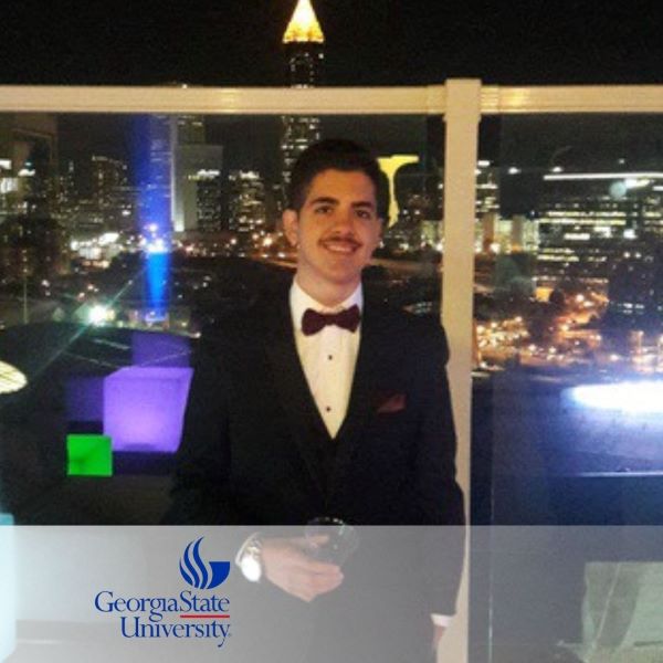 Adonis Aviles-Gonzalez, smiling and holding a glass with a city skyview in the background.