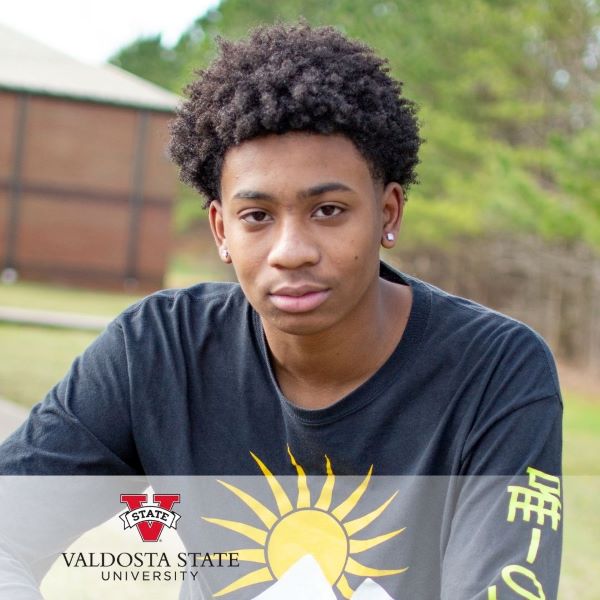 Cemaurion Moore, in a headshot in an outdoor setting.