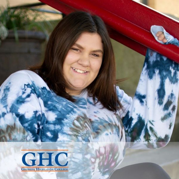 Kayla Linard, smiling and wearing a long sleeve tie die shirt in an outdoor setting.