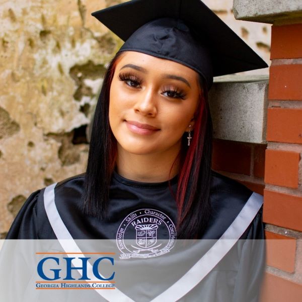 Kayleen Uriostegui, wearing a black cap and gown, leaning against a brick wall.